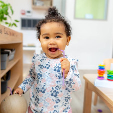 enfant qui sourit dans la crèche entouré de jouets et meubles en bois 